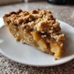 Ein Stück Klassischer Zwetschgenkuchen Streusel Genuss auf einem weißen Teller, mit saftiger Füllung und knusprigen Streuseln.
