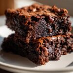 Zwei saftige Brownies mit Schokoladenstückchen gestapelt auf einem Teller, ein wahrer Schoko Genuss.